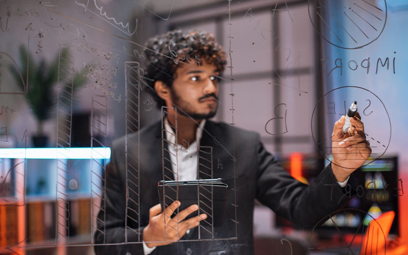 A professional man in a suit writing on a glass wall with a marker.