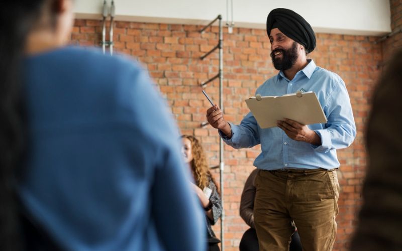 A man in a turban presenting to a group of people in a meeting room.